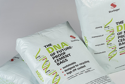 Mehrere Zementsäcke von Starlinger, gestaltet in hellgrüner Farbe, mit der Aufschrift 'The DNA of future-proof cement bags'. Auf den Säcken ist eine stilisierte DNA-Helix abgebildet, die Eigenschaften wie 'strong', 'economical', 'recyclable' und 'sustainable' hervorhebt. Das Starlinger-Logo befindet sich oben rechts auf jedem Sack.