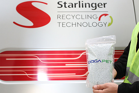 The image shows a close-up of a Starlinger PET recycling machine, with hands holding a bag of recycled PET granules. The machine's logo, "Starlinger recycling technology," is visible in the background, along with red design elements. The bag is labeled "DOGAPET" and contains small white plastic granules, which are the recycled PET material produced by the machine. The person holding the bag is wearing a high-visibility safety vest.